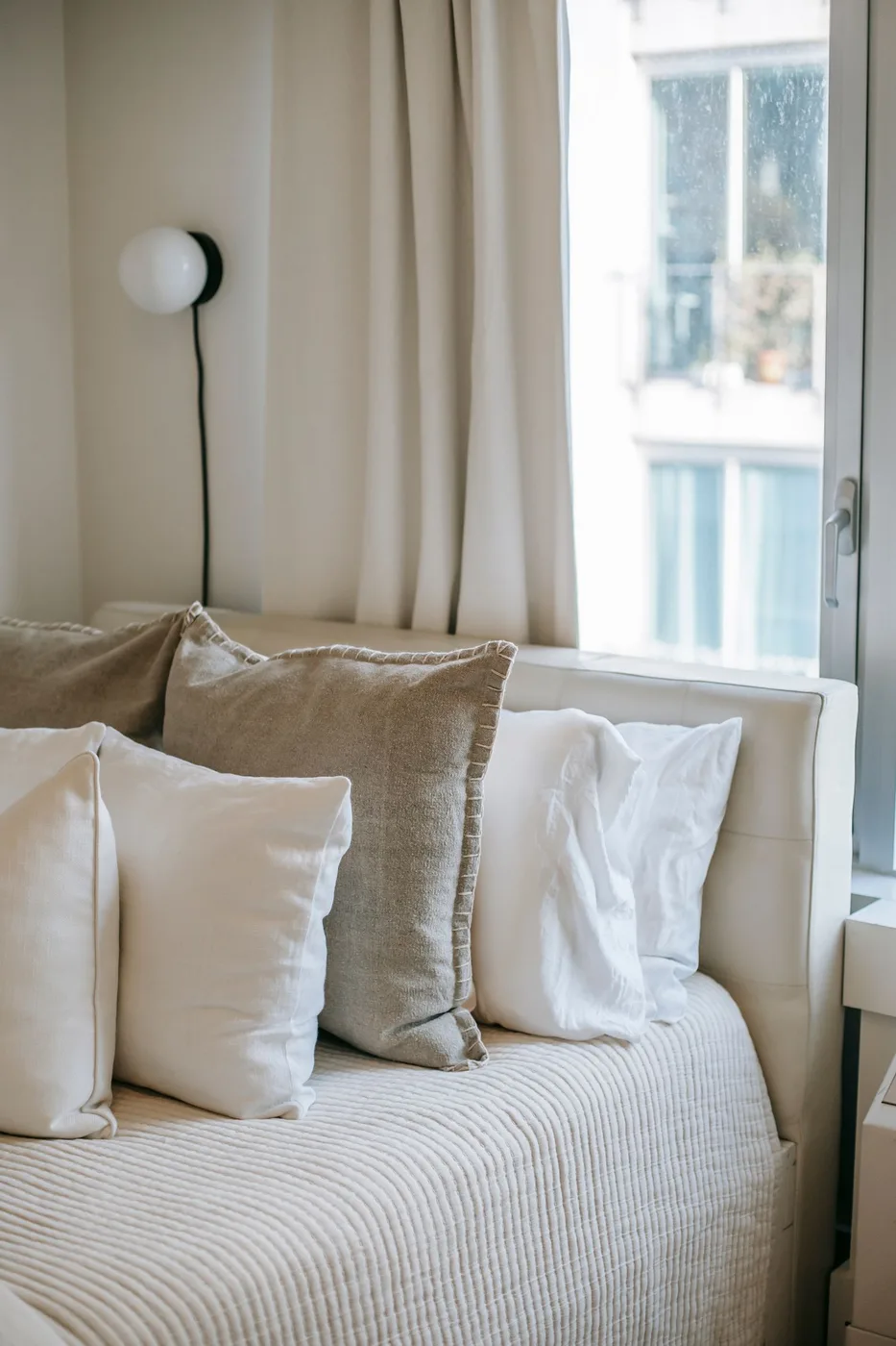 A sunlit bedroom with soft natural textiles and a thoughtfully arranged bed