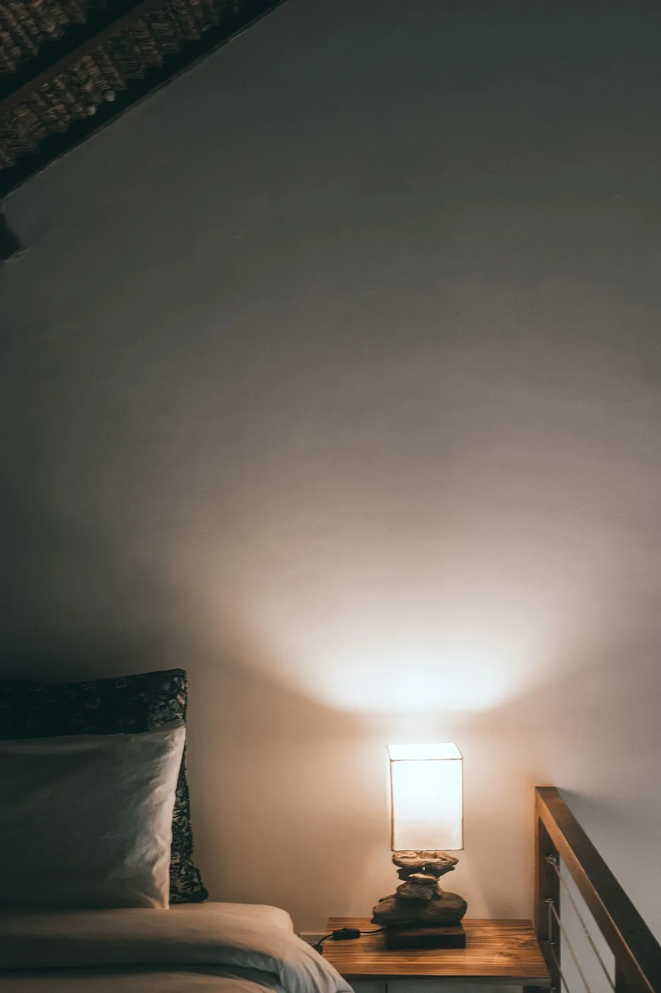 A lamp on a nightstand beside a neatly made bed